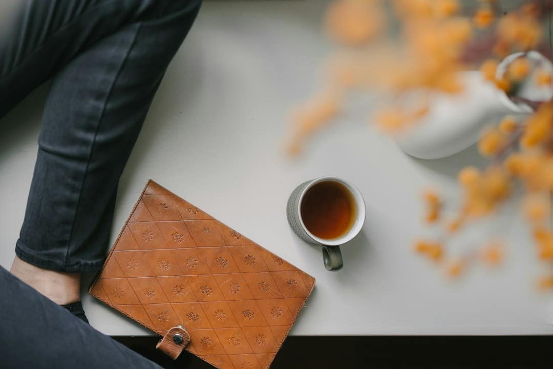Dark pants and black socks near a leather portfolio and tea.